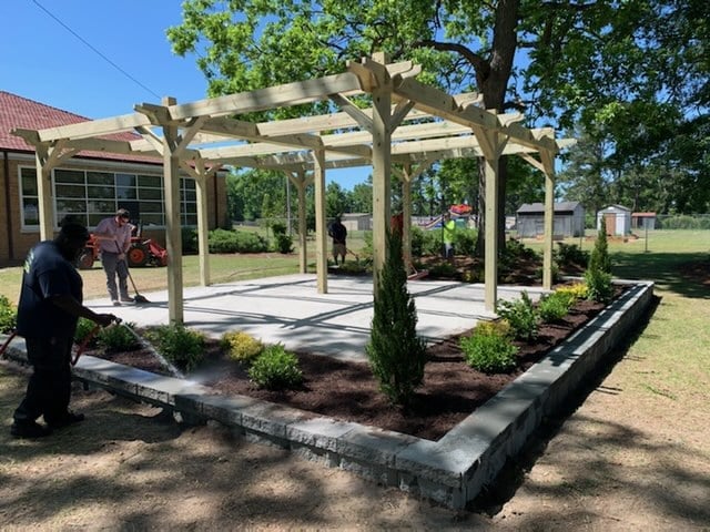 Wooden pergola structure with concrete patio and landscaping in a residential outdoor space